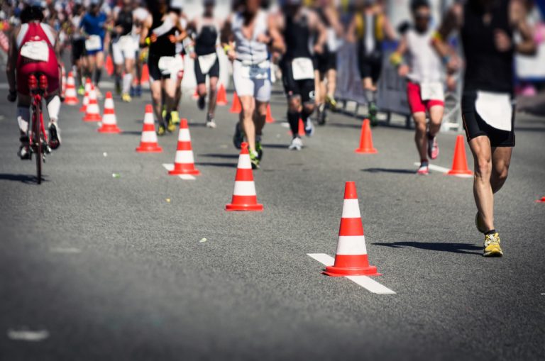 Running competition in an ironman event with runners and a biker traversing a highway.